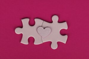 Two puzzle pieces, connected with a heart shape over them