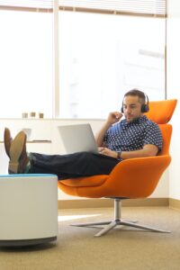 A man sitting in a chair, listening to music on a laptop